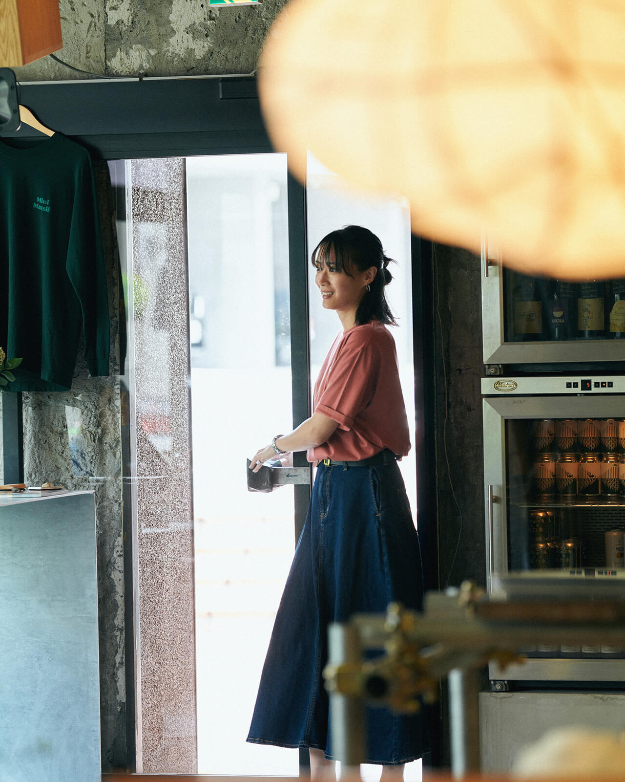 ピンクのトップス・ブルーデニムのスカートを着用した女性がカフェの出入り口付近にいる様子