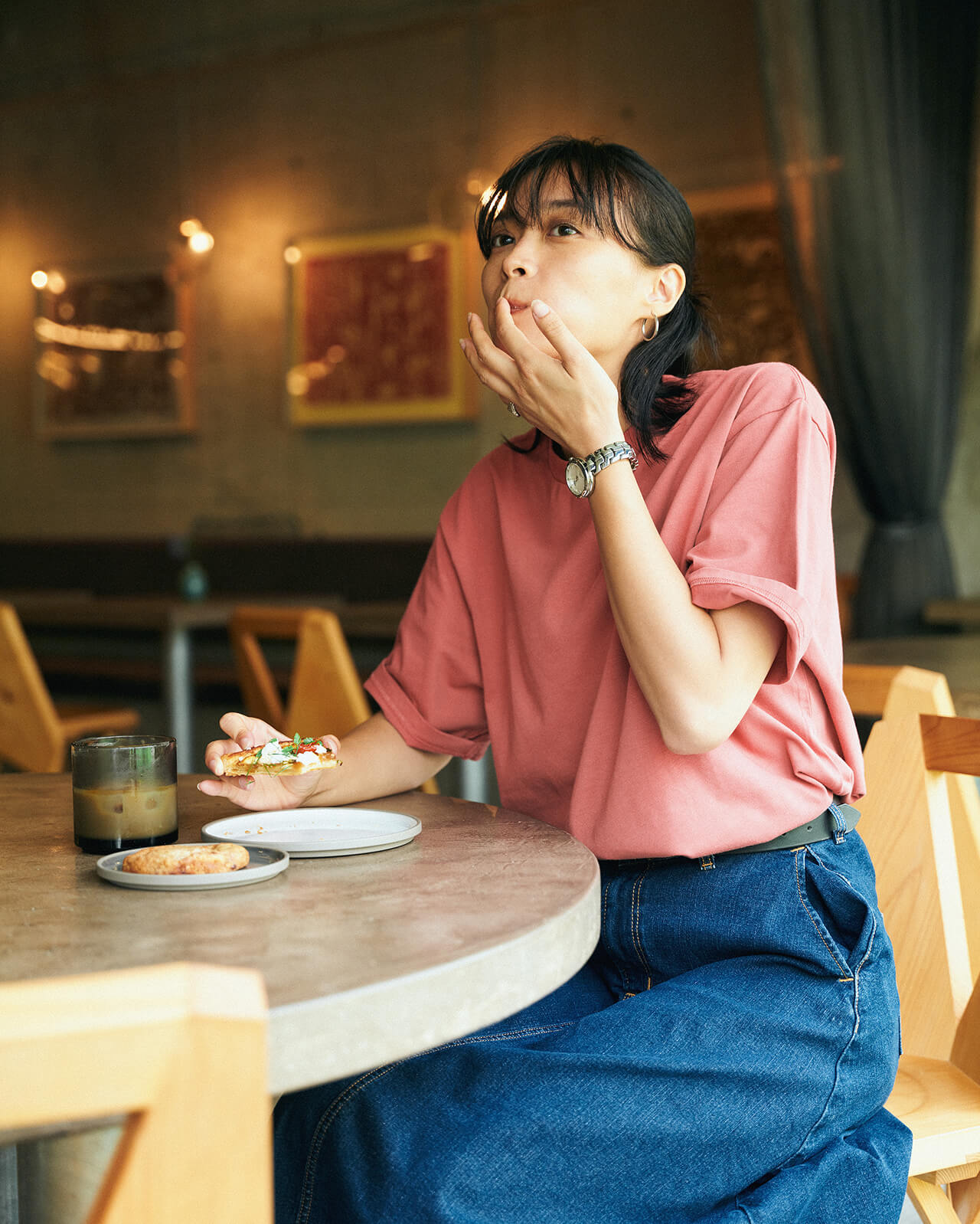 ピンクのトップス・ブルーデニムのスカートを着用した女性がピザを食べている様子