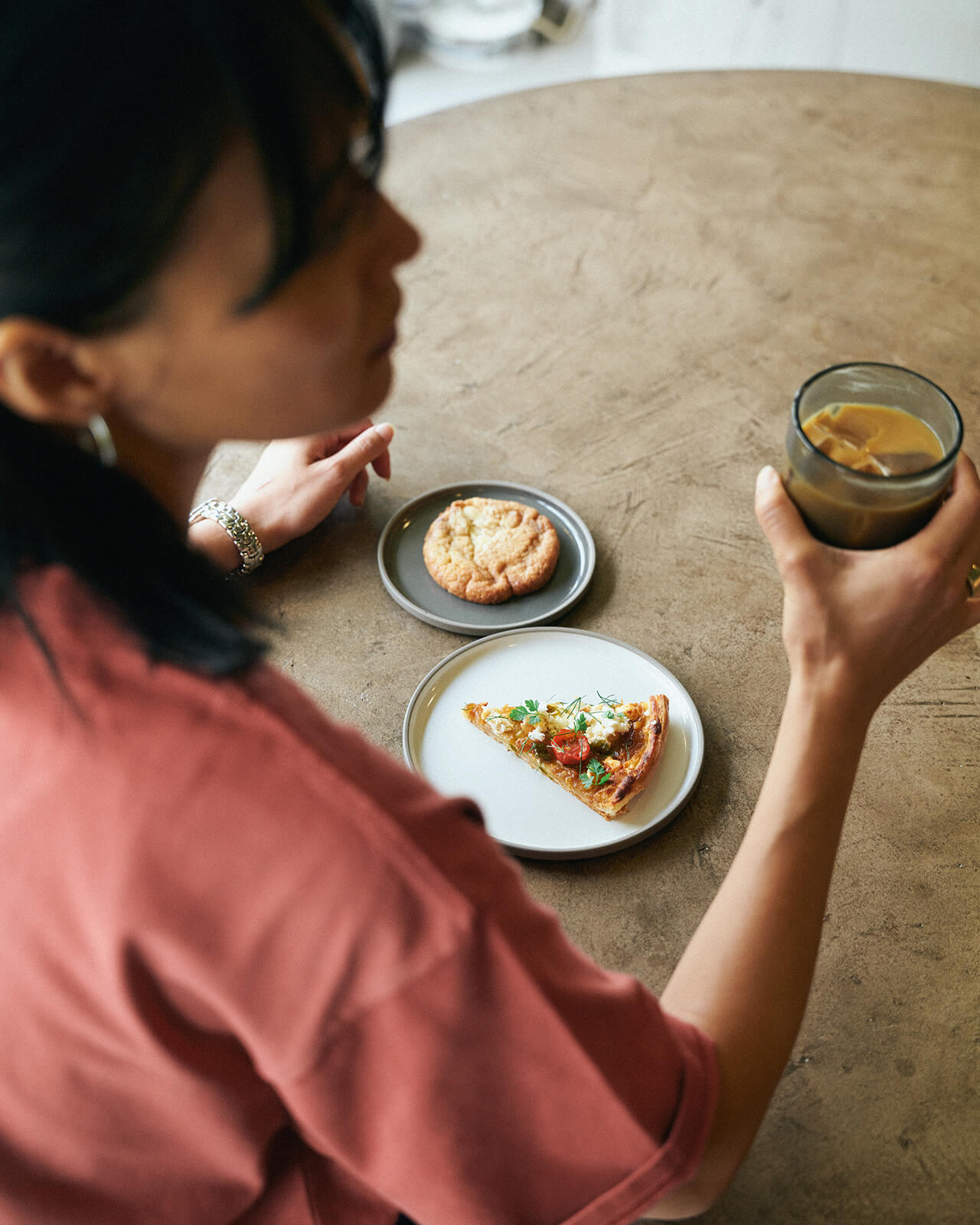 ピンクのトップス・ブルーデニムのスカートを着用した女性がカフェラテを飲もうとしている様子