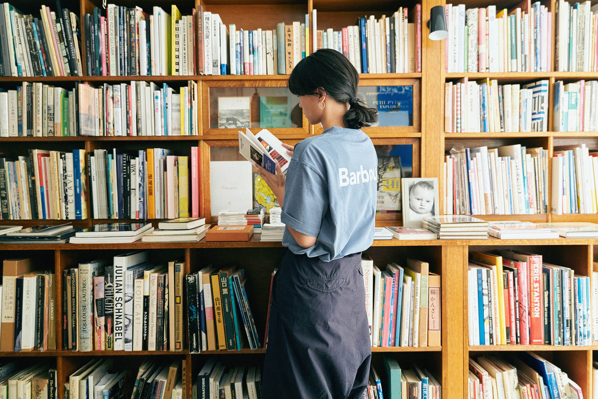 ライトブルーのトップス・ネイビーのボトムスを着用した女性が本屋さんで本を立ち読みしている様子