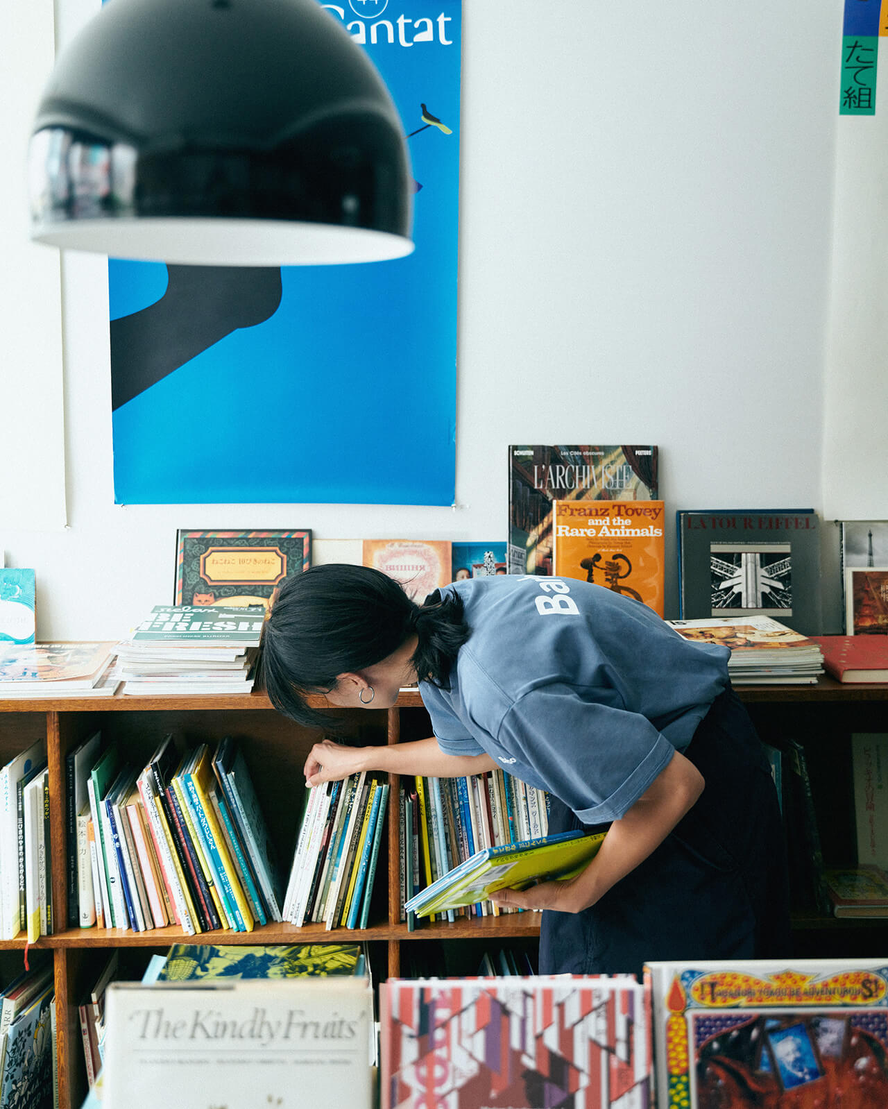 ライトブルーのトップス・ネイビーのボトムスを着用した女性が本屋さんで本を選んでいる様子