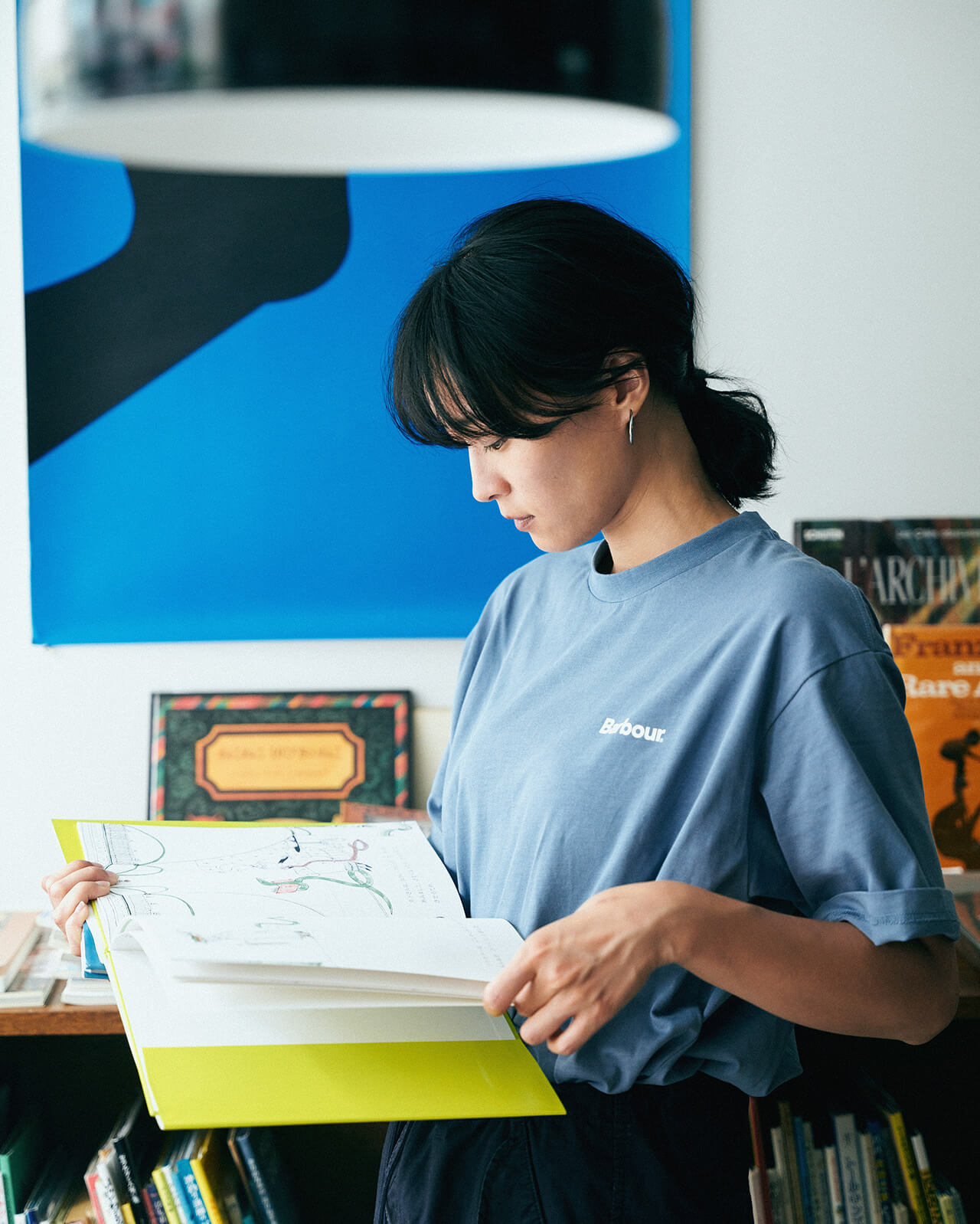 ライトブルーのトップス・ネイビーのボトムスを着用した女性が本屋さんで本を立ち読みしている様子