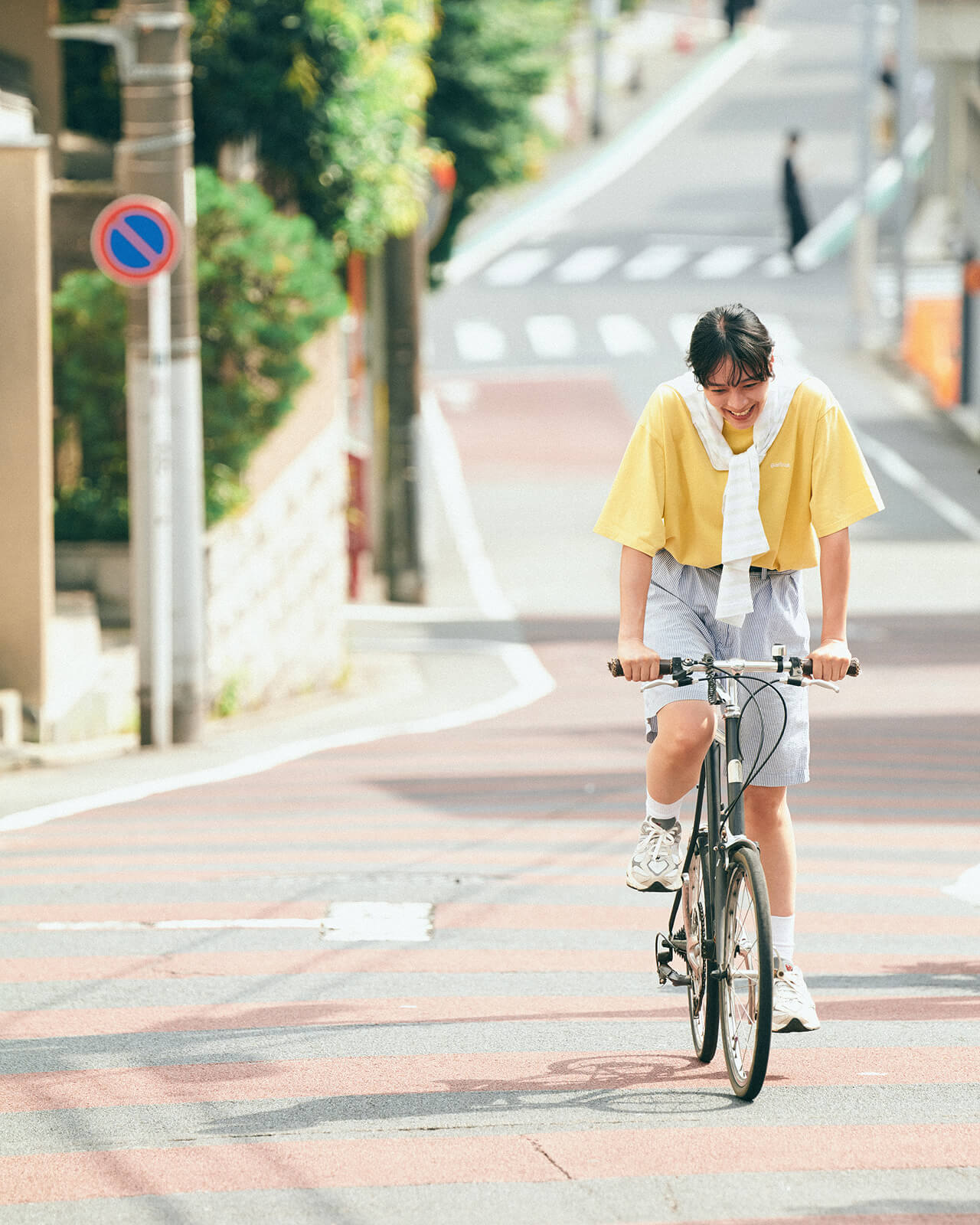 イエローのトップス・ボーダーのハーフパンツを着用した女性が自転車に乗って坂を登っている様子