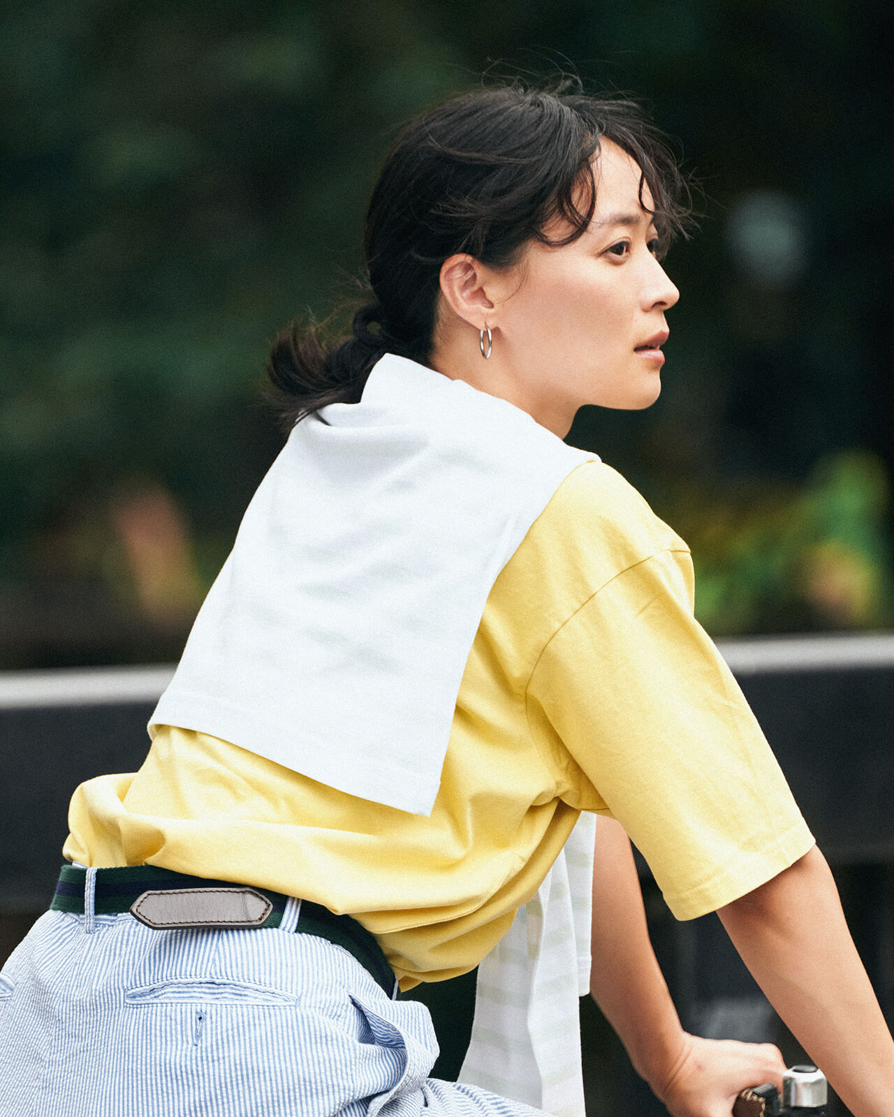 イエローのトップス・ボーダーのハーフパンツを着用した女性が自転車に乗って遠くを眺めている様子