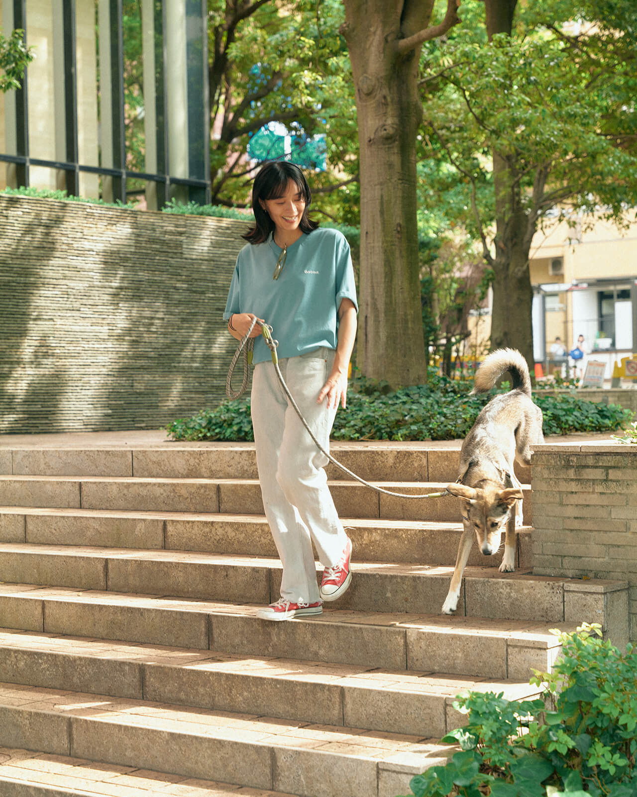 ライトブルーのトップス・デニムパンツを着用した女性が犬と散歩している様子