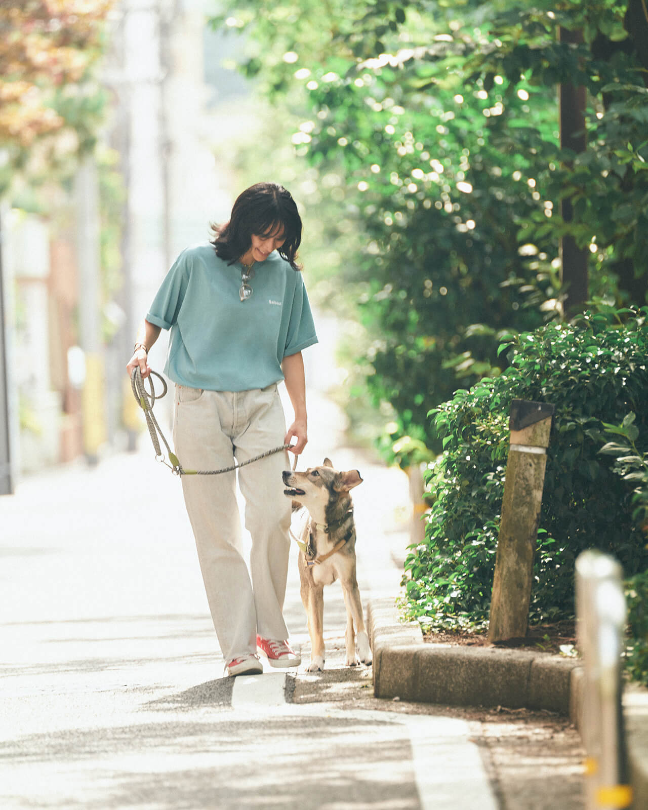ライトブルーのトップス・デニムパンツを着用した女性が犬と散歩している様子