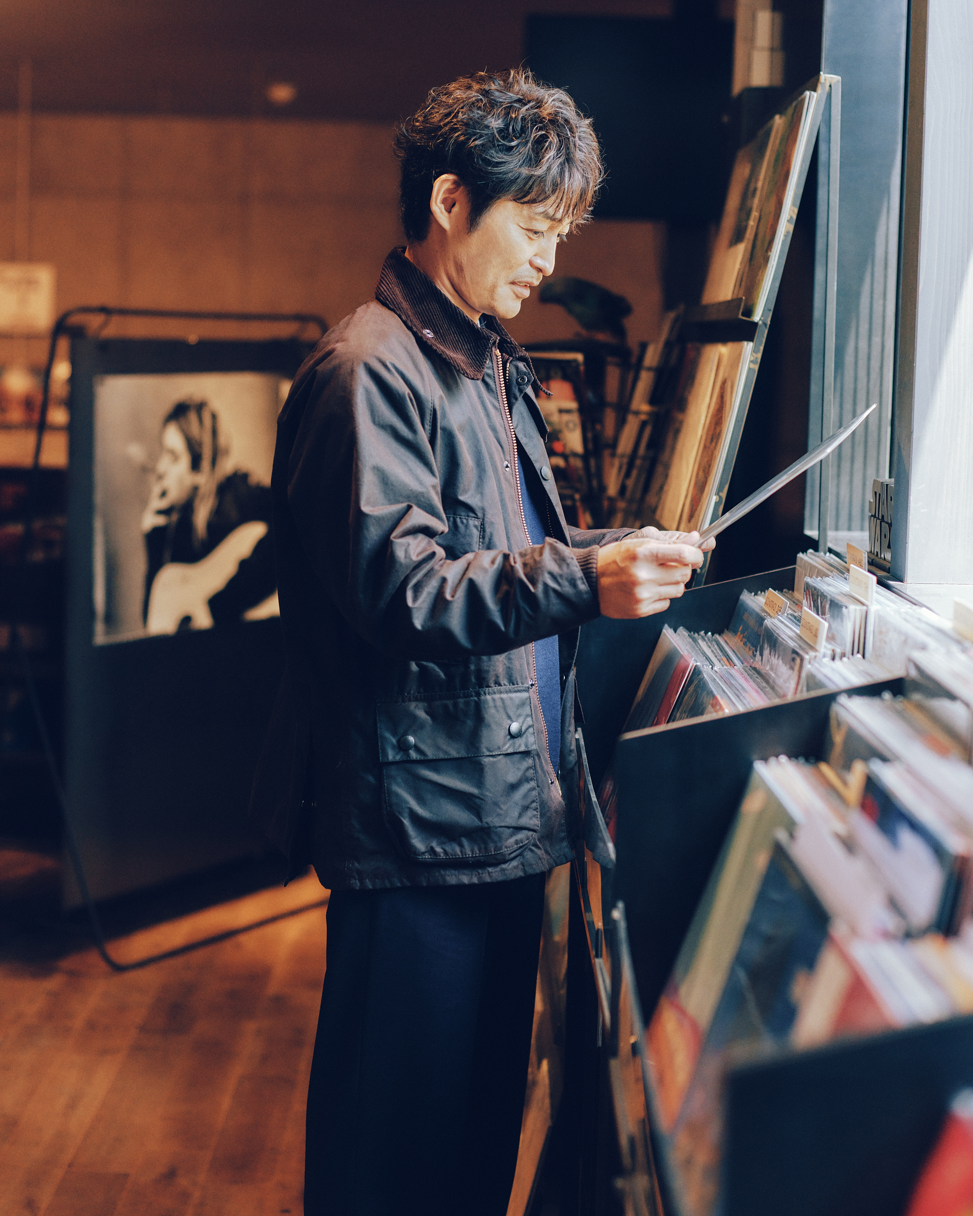 レコード店「ボイラーレコード」でBarbourのブラックのジャケットを着用した男性がレコードを選んでいる様子